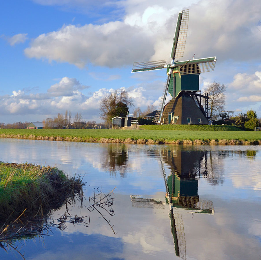 De Kockengense Molen met een mooie wolkenpartij in de bovenste helft van de foto en in de onderste helft de weerspiegeling van de molen in de sloot.