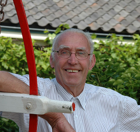 Foto van Piet Brandhorst. Hij is een witte man met grijs haar en bril en lacht op de foto. Met zijn elleboog leunt hij op één van de spaken van het kruirad van de molen.